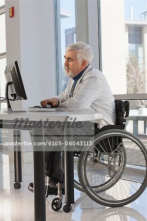 Doctor with muscular dystrophy in wheelchair studying information on his computer