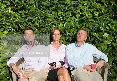 Three businesspeople sitting on bench, asleep