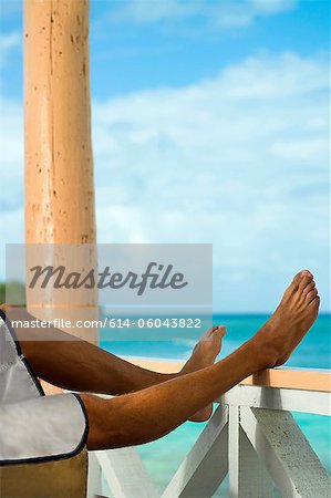 Man on vacation with legs resting on veranda rail