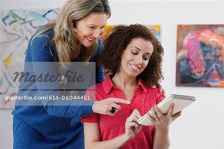 Mid adult woman advising art student drawing in sketch pad in art gallery