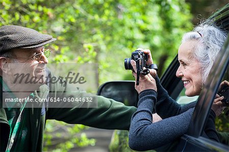 Senior woman photographing man from car