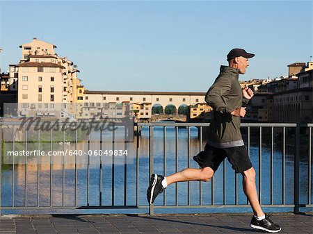 Italy, Florence, Man jogging past Ponte Vecchio over River Arno
