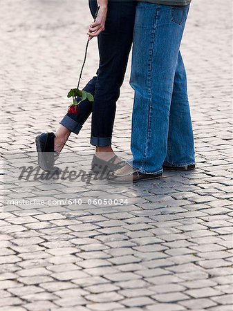 Italy, Rome, Vatican City, Close up of legs of couple with rose standing on cobblestone