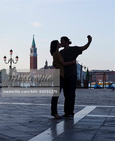 Italy, Venice, Young couple kissing and photographing self, San Giorgio Maggiore church in background
