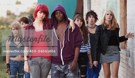 A pair of young punk teens pose together as their friends stay in the background.