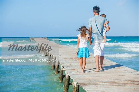 Family of three on wooden jetty by the ocean. Back view