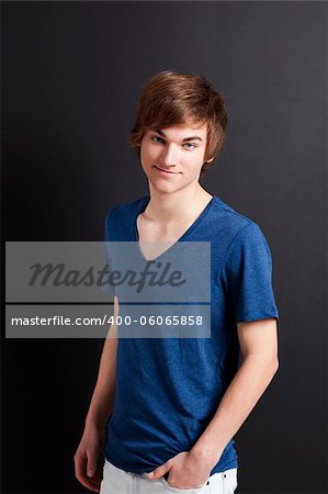 Portrait of a casual young man with a happy face, against a black wall