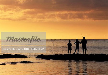 Three young fishermen are on the beach at sunset.