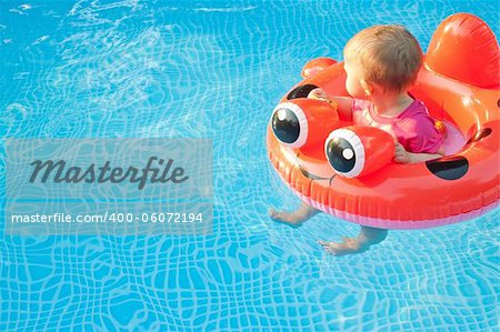 Small child in floatation device looking away while floating in a pool alone