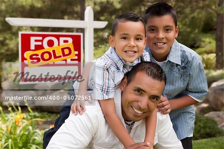 Hispanic Father and Sons in Front of a Sold Home For Sale Real Estate Sign.