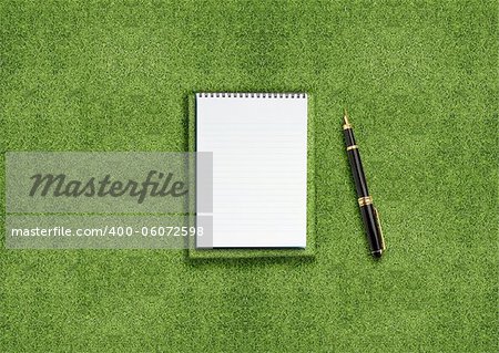 blank opened notebook outdoors on the green grassland and pen
