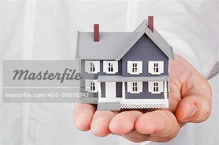 Close-up photograph of a miniature house in a man's hand.