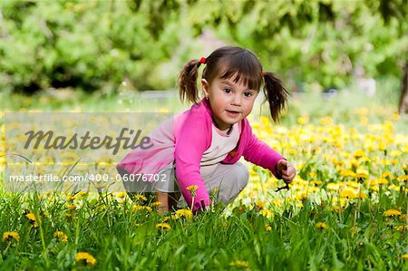 A little girl wearing a pink shirt, sitting on the dandelion field
