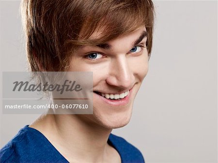 Portrait of a handsome young man smiling to the camera, over a gray background