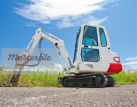 Small caterpillar tractor stands on the asphalt against the blue sky