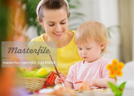 Mom helping baby painting on Easter eggs