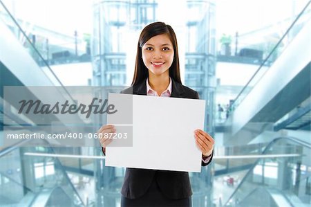Mixed race Asian businesswoman holding a white board standing inside modern building.