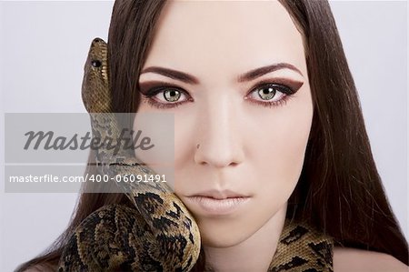 beautiful brunette girl with a snake around her head stares at the viewer