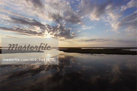 The sun rising behind clouds is reflected in the water of the marshes near the Bodie Island lighthouse at Cape Hatteras National Seashore on the Outer Banks of North Carolina
