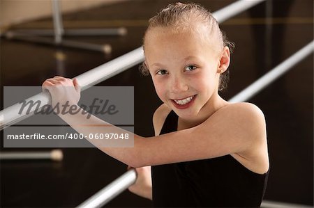 Smiling ballerina girl holding balance bars in dance studio