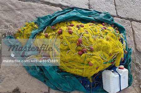 Yellow fishing nets pine, ropes and canister on stone paved ground