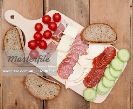 Snack - Salami, Cheese, Vegetables and Bread on Wooden Chopping Board