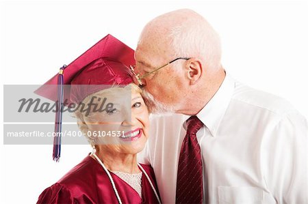 Senior woman earns a college degree and a kiss from her husband.  Isolated on white.