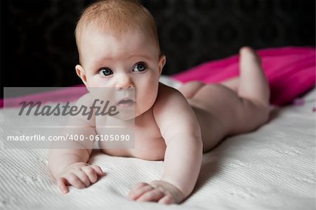 cute healthy infant with no diaper lying on a white woolen plaid and looks away in surprise against the backdrop of a pink curtain