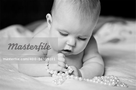 Pretty girl plays with infant enthusiasm pearl beads lying on tummy picture black and white