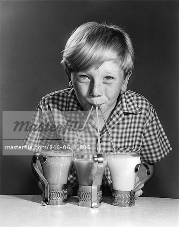 1950s 1960s PORTRAIT OF BLONDE BOY DRINKING WITH STRAWS FROM 3 MILKSHAKES SODAS SMILING LOOKING AT CAMERA