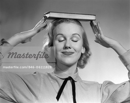 ANNÉES 1950 FEMME BLONDE SOURIANTE AVEC DES YEUX FERMÉS ÉQUILIBRAGE LIVRE SUR SA TÊTE