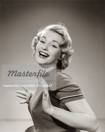 1950s YOUNG WOMAN SMILING WITH BOTH THUMBS TUCKED UNDER HER ARM LOOKING AT CAMERA