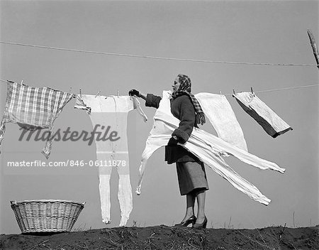 1950s HOUSEWIFE REMOVING FROZEN LONG JOHNS FROM CLOTHESLINE