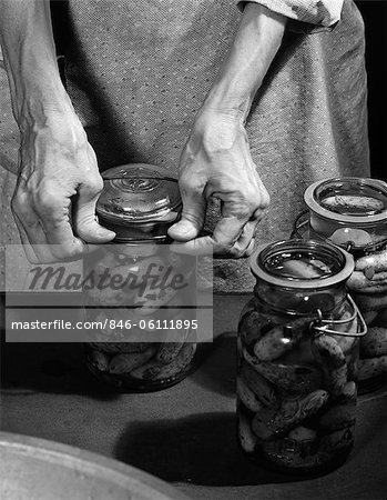 1950s CLOSE-UP OF ELDERLY WOMAN'S HANDS SEALING LID ON JAR OF HOME-MADE PICKLES
