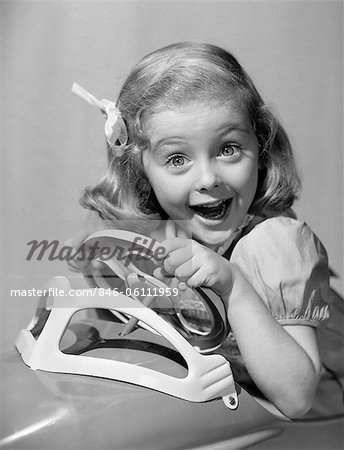 1950s PORTRAIT OF LITTLE GIRL DRIVING TOY CAR WITH EXCITED EXPRESSION LOOKING AT CAMERA