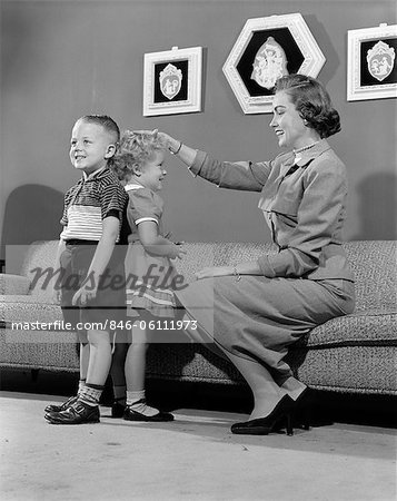 1950s MOTHER MEASURING DIFFERENCE IN HEIGHT BETWEEN SON AND DAUGHTER INDOOR