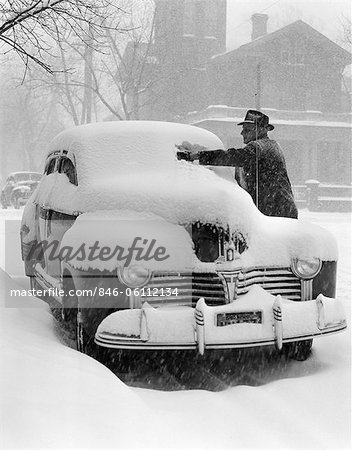 1940s MAN REMOVING SNOW FROM WINDSHIELD OF PARKED CAR