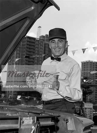 PRÉPOSÉ DE STATION-SERVICE SOURIANT DES ANNÉES 1960 EN UNIFORME ESSUYER LA JAUGE APRÈS VÉRIFICATION DE L'HUILE