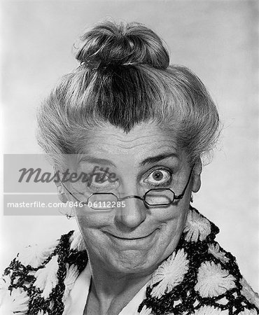 ANNÉES 1970 PORTRAIT FEMME ÂGÉE AVEC DES CHEVEUX EN CHIGNON PORTANT GRANNY LUNETTES SOURIANTE REGARDANT LA CAMÉRA