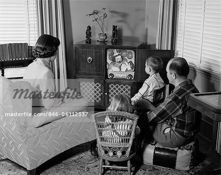 1950s BACK VIEW OF FAMILY OF 4 GATHERED AROUND TV SET WATCHING CLOWN WITH BALLOONS