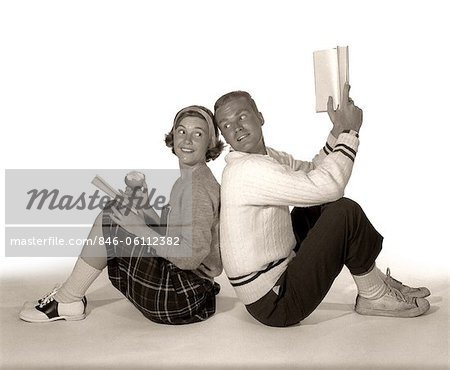 1960s TEEN MALE & FEMALE BACK TO BACK LOOKING TOWARDS EACH OTHER STUDYING