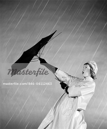 1950s WOMAN IN RAIN COAT TRYING TO USE BROKEN UMBRELLA  IN THE WIND