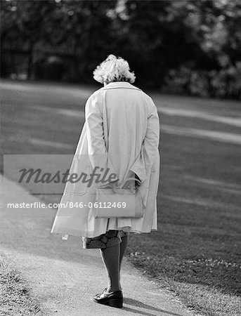 1980s REAR VIEW OF ELDERLY WOMAN WALKING DOWN SIDEWALK HOLDING PURSE BEHIND BACK HEAD DOWN