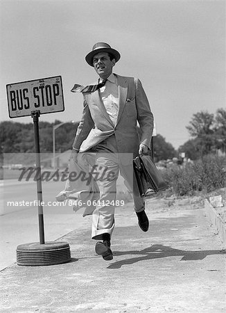 1950s SALESMAN RUNNING TO CATCH BUS AT BUS STOP SIGN OUTDOOR