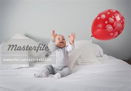 Baby boy playing with balloon on bed