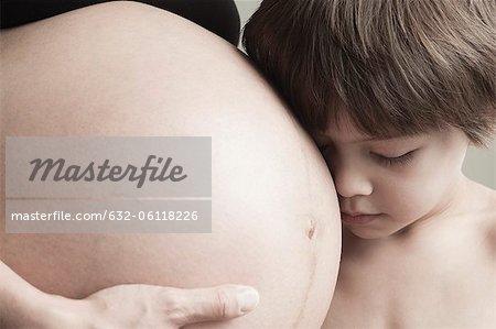 Boy resting head on mother's pregnant belly, cropped