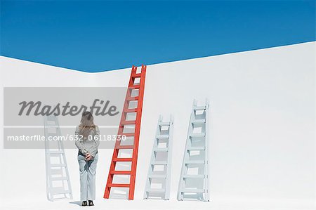 Businesswoman contemplating ladders, rear view