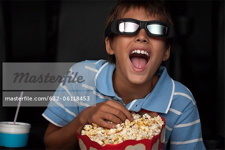 Boy laughing and eating popcorn during 3-D movie in theater