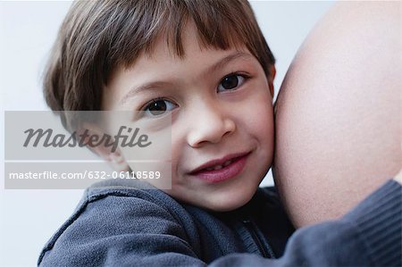 Boy hugging mother's pregnant belly, cropped