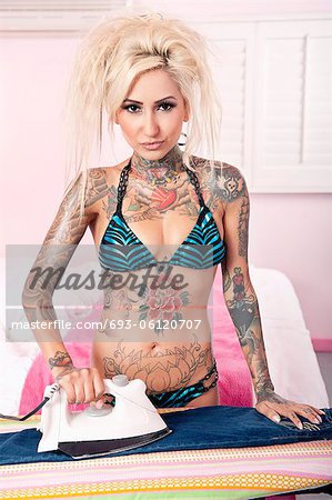 Portrait of young tattooed woman ironing in bedroom